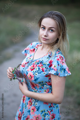 Young beautiful woman in flower vintage dress holding flowers in her hands on the background of green field.