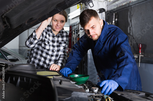 Man and woman workers are replacing the oil in the car