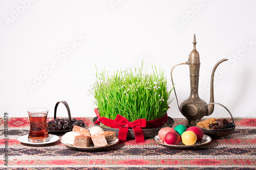 Novruz setting table decoration, tea in  tulip shape glass on ethnic motives rustic table cloth with wheat grass, dyed eggs, traditional sweets, samovar, new year sring celebration, nature awakening photo