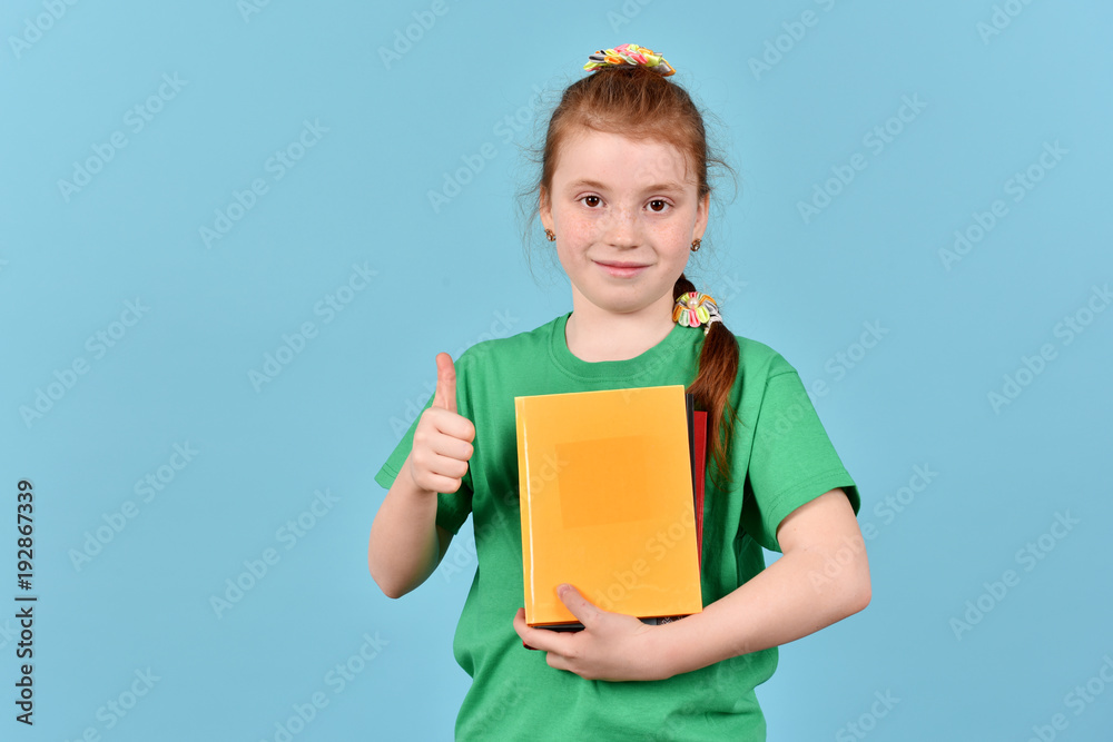 Obraz premium Schoolgirl with a book. A girl on a blue background. Isolated children.
