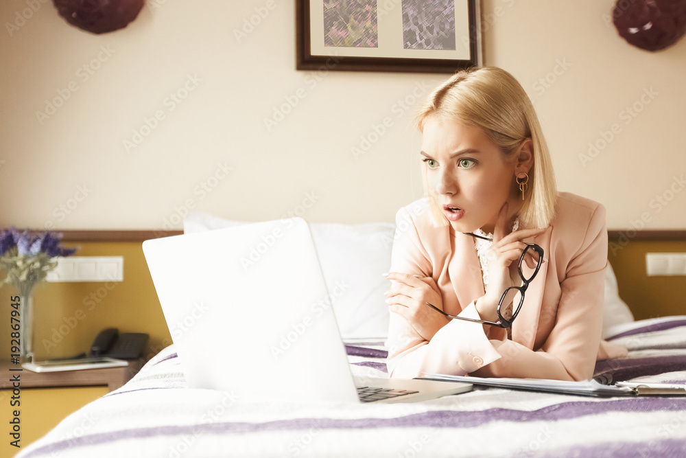 Shocked businesswoman lying on bed and using tlaptop Shocked businesswoman lying on bed and using tlaptop