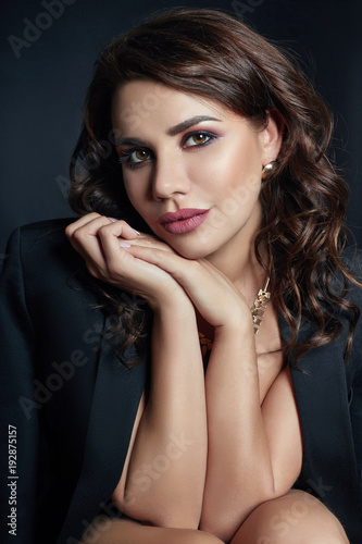 Sexy brunette with beautiful curly hair in an erotic black jacket. Expensive jewelry and smooth natural pure skin. Beautiful evening makeup  fashion portrait of a woman
