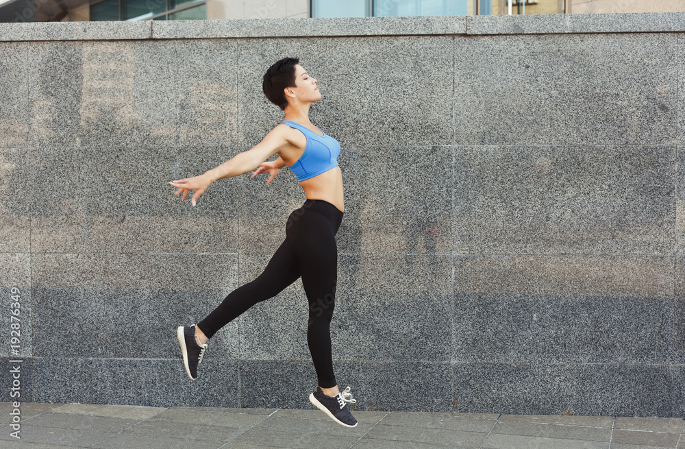 Fototapeta premium Beautiful young woman jumping against brick wall
