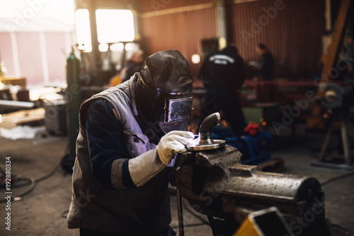 Welder in protective uniform and mask welding metal pipe on the industrial table while sparks flying. © dusanpetkovic1