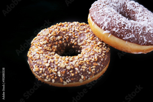 Assorted doughnuts in the glaze, colorful sprinkles and nuts on a black background.