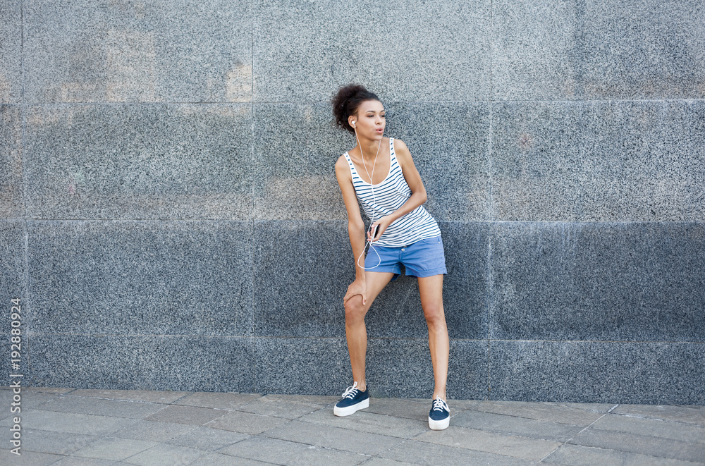 Tired woman runner is having break, standing near grey wall