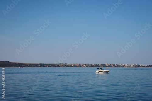 Motorboat sailing on the sea, quiet cruise on the blue water, active rest summer vacation. Pier city background © ANR Production