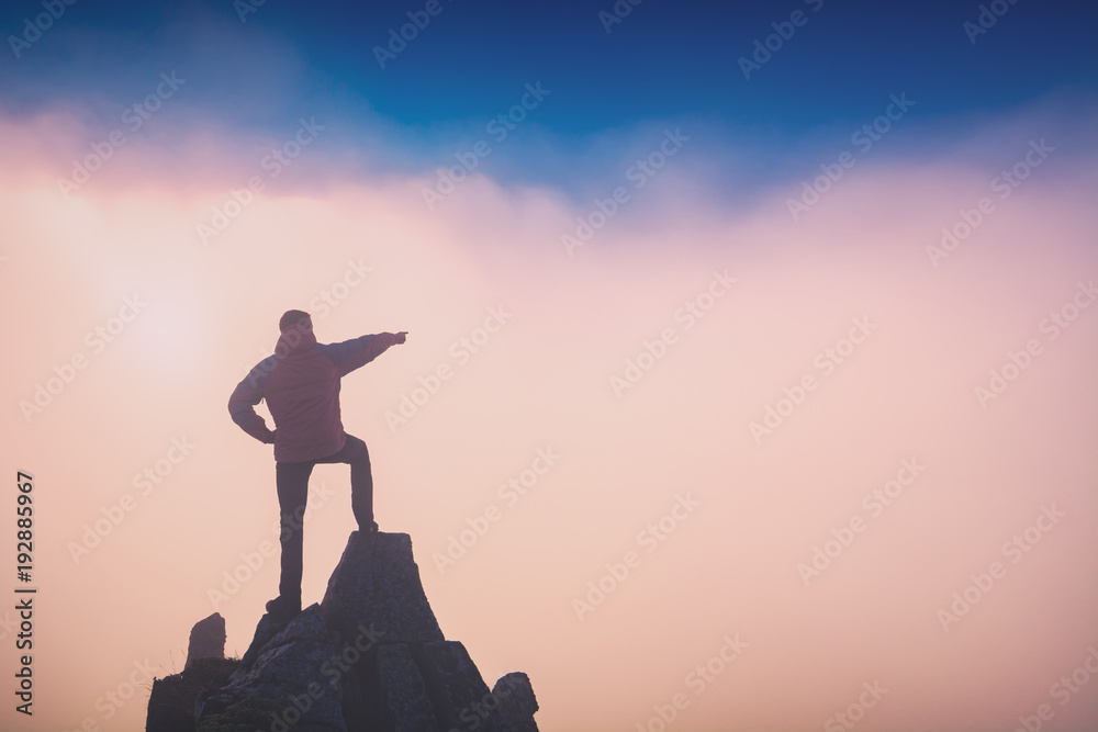 Hiker standing on a rocky cliff and points to the sky