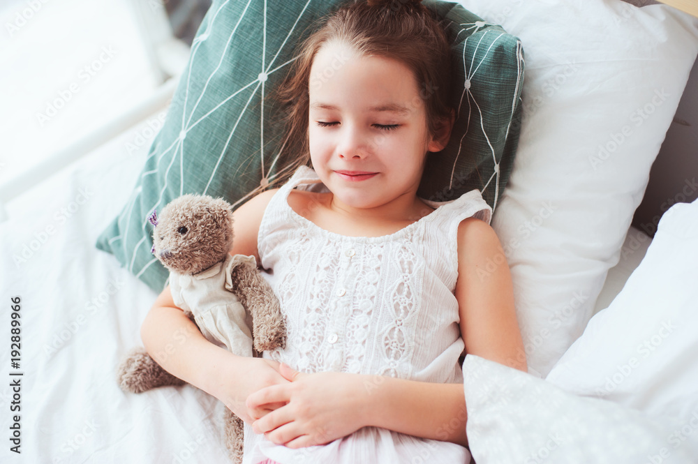 cute little child girl sleeping and watching sweet dreams with her teddy bear in comfortable bed.