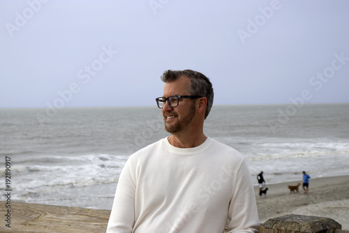 Folly Beach South Carolina, February 17, 2018 - white male model wearing long white shirt looking into the distance with ocean waves behind him