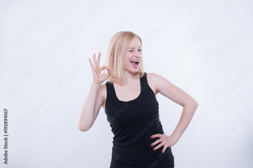 Woman makes ok sign with her hand and beaming. Expressive facial expression and emotion. Portrait of pretty blonde girl smiling isolated on white background. Woman makes ok sign with her hand and beaming. Expressive facial expression and emotion. Portrait of pretty blonde girl smiling isolated on white background.