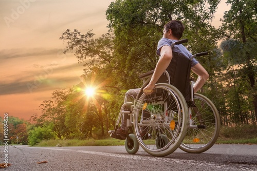 Disabled or handicapped young man on wheelchair in nature at sunset.
