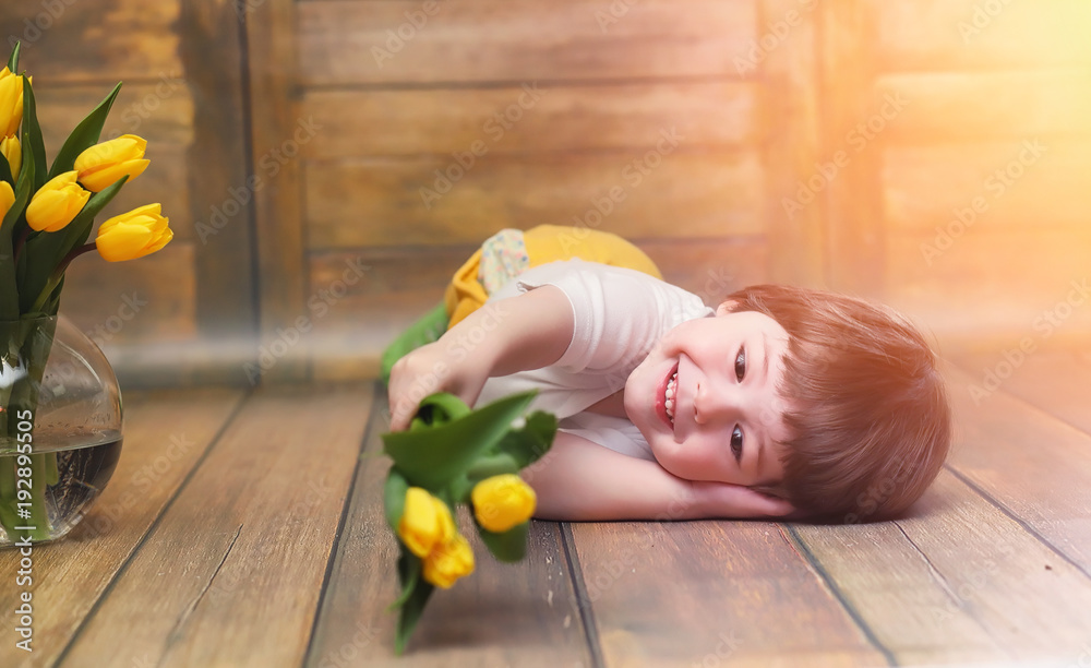 Fototapeta premium A small child with a bouquet of yellow tulips. A boy with a gift