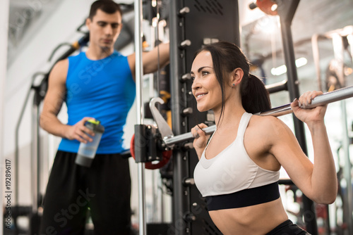 Portrait of beautiful young woman smiling happily while training with barbell in modern gym, copy space