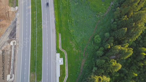Aerial view at the country highway passing near forest in evergreen northern forests. Clip. Top view of the motorway near the forest