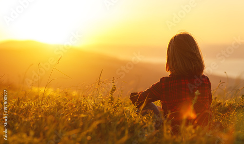 Woman sits with her back in the field and look sunset in the mountains photo