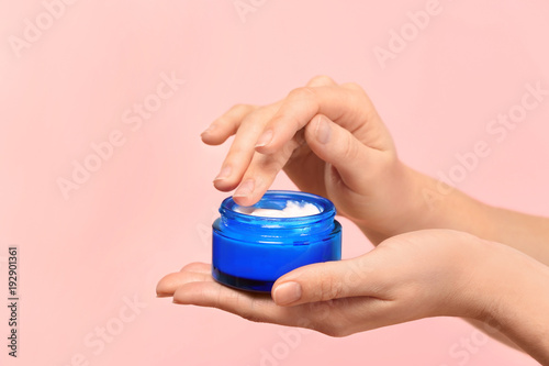 Woman with jar of body cream on color background