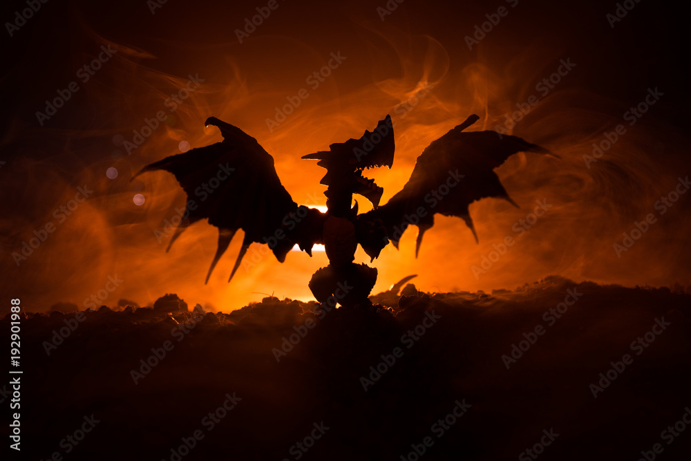 Naklejka Silhouette of fire breathing dragon with big wings on a dark orange background