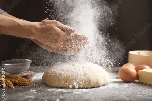 Photo Woman clapping hands and sprinkling flour over fresh dough on table