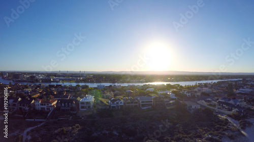 Early morning drone aerial view of South Australian beach with sun rising over Adelaide Hills and West Lakes, and Tennyson homes overlooking the sea.