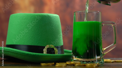 St Patrick's Day pouring green beer with green leprechaun hat and gold covered chocolate coins against rustic wood background photo