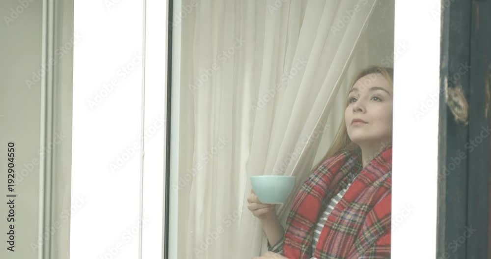 Beautiful young woman drinking coffee and looking through window. Beautiful young woman drinking coffee and looking through window.