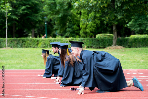 Graduation group of students celebrating on athletic track, preparing to race. Students competiting in a race on athletic track after graduating.