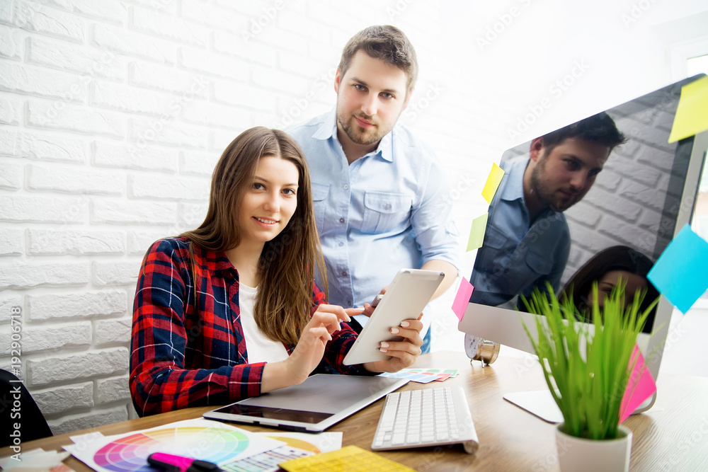 Beautiful young designers discussing ideas and smiling while working in office Beautiful young designers discussing ideas and smiling while working in office