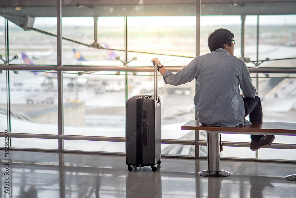Young Asian man sitting on bench in the airport terminal with suitcase luggage, travel lifestyle Young Asian man sitting on bench in the airport terminal with suitcase luggage, travel lifestyle