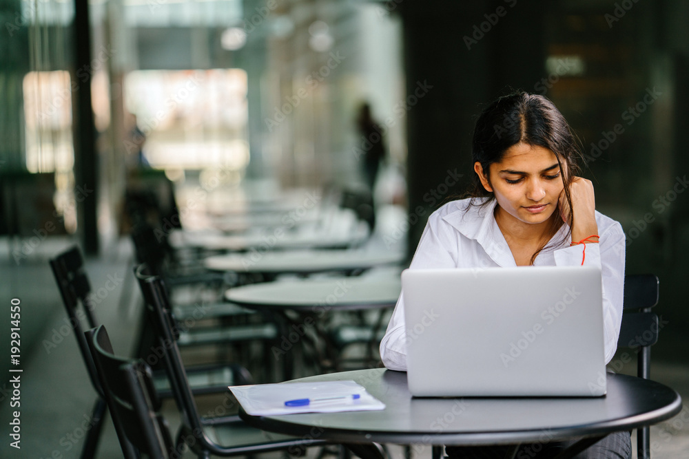 A young job seeker is applying on her laptop computer for her job. It is a portrait of a young and attractive Indian lady sitting at a table, smiling and filling in her application. A young job seeker is applying on her laptop computer for her job. It is a portrait of a young and attractive Indian lady sitting at a table, smiling and filling in her application.