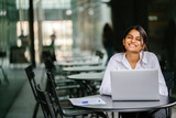 A young job-seeker applies for her job on her laptop computer. It is a portrait of a young and attractive Indian lady sitting at a table as she smiles and fills in her application.