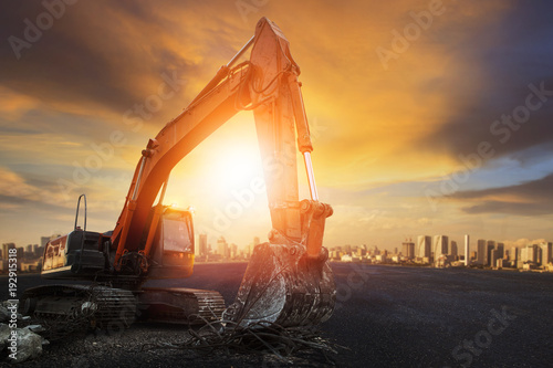 articulated wheel bucket tractor on asphalt ground with sunset sky and urban building scene