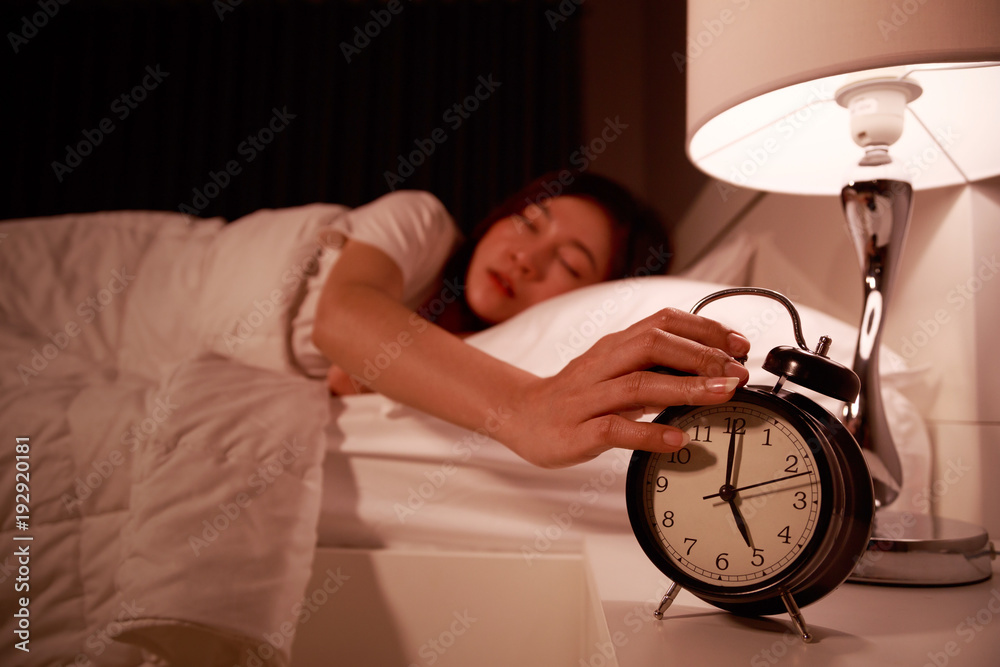 Φωτογραφία sleepy woman in bed with eyes closed extending hand to alarm clock in the mornin