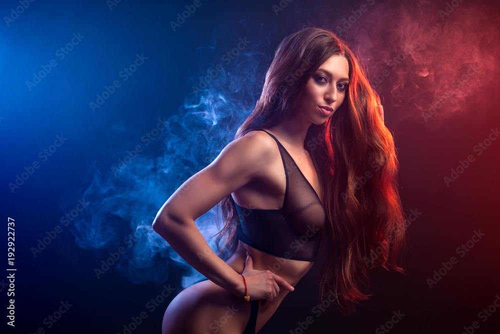Young  beatiful woman in black underwear posing against a background of  blue  and red smoke from a vape on a black isolated background