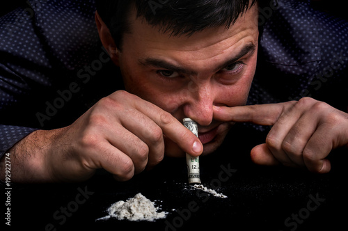 Junkie man snorting cocaine powder with rolled banknote