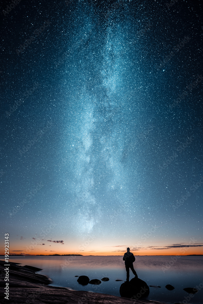 Φωτογραφία Silhouette of a man standing alone on a rock by a sea and looking at sunset and