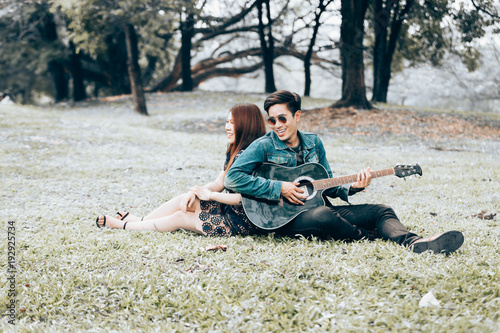 Asian couple in love playing acoustic song  guitar sitting on grass in the park © kasipat