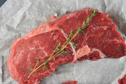 Raw beef steak on parchment paper. On the steak is a twig of thyme. View from above. Close-up. Macro photography.