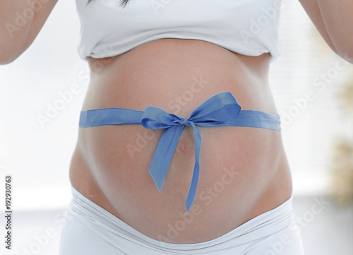 Wallpaper Mural close up of a smiling pregnant woman tying a blue ribbon on her tummy. Torontodigital.ca