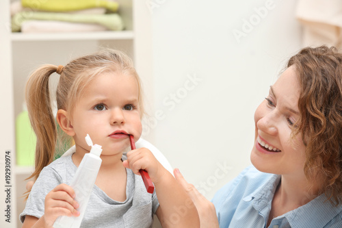 Mother teaching daughter to brush teeth in bathroom
