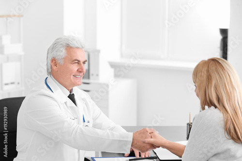 Male doctor and patient shaking hands during consultation in clinic