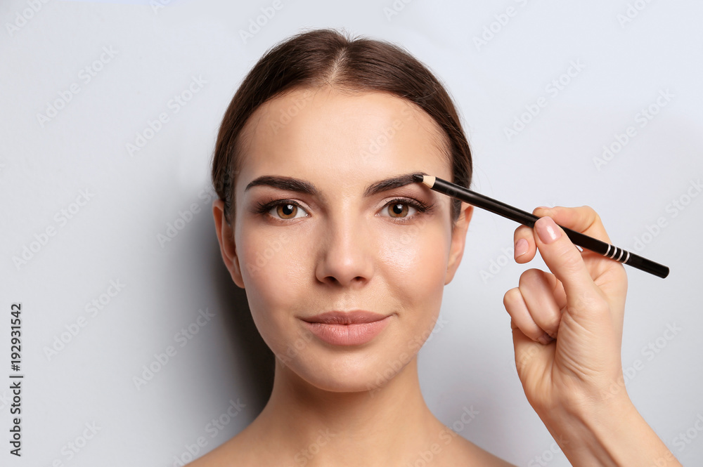 Fototapeta premium Young woman undergoing eyebrow correction procedure on light background