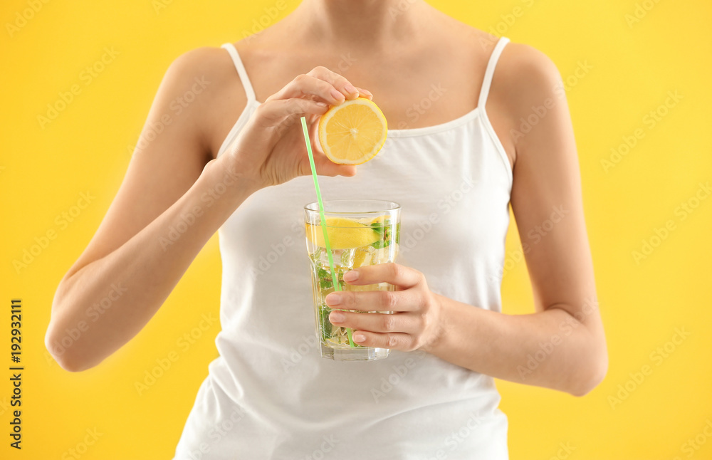 Young woman squeezing juice into glass with lemonade on color background Young woman squeezing juice into glass with lemonade on color background