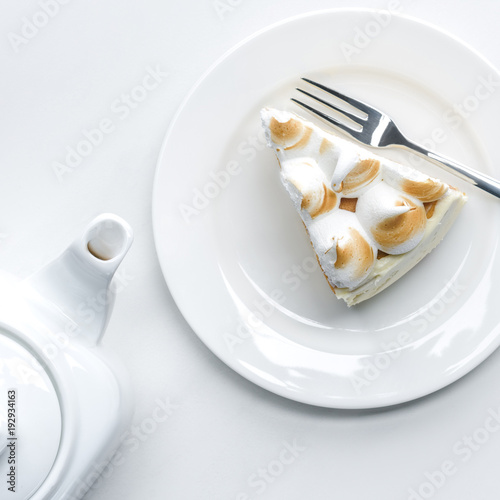 top view of delicious piece of cake with meringue and teapot on white table