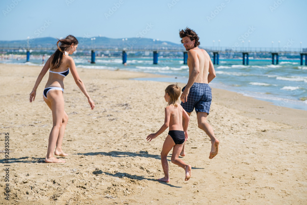 Mom, dad and son run along the beach to the pier in swimming trunks. Beach holiday.