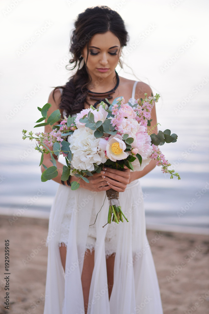 bride in a boho style on the beach near the sea with a wedding bouquet bride in a boho style on the beach near the sea with a wedding bouquet