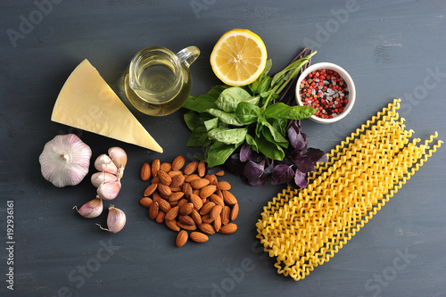 Ingredients for pasta with pesto sauce. In the frame, green and purple basil, almonds, half a lemon, parmesan cheese, garlic, spices, olive oil and pasta Fusilli lunghi. Close-up. View from above. photo