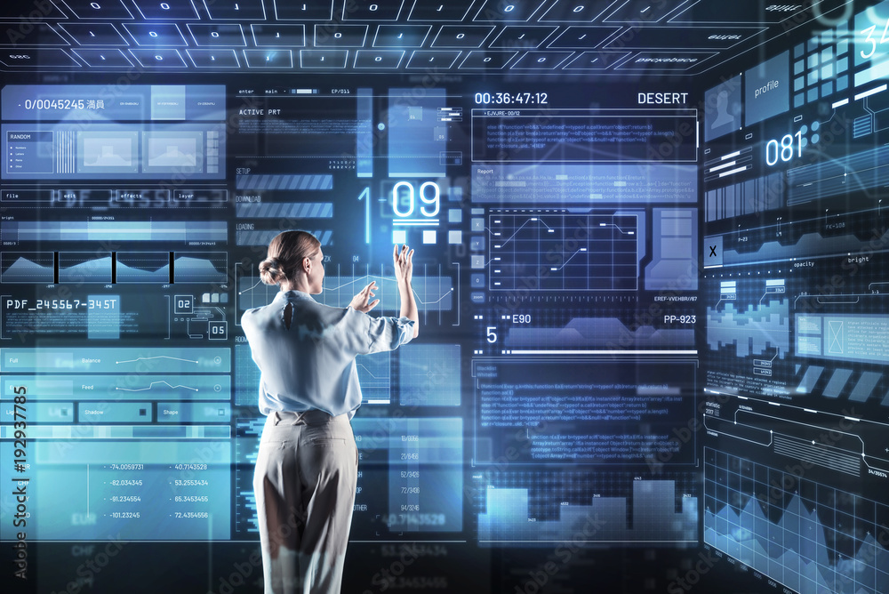 Fototapeta premium Convenient device. Clever qualified young programmer feeling confident while standing in her modern office and working with a giant futuristic transparent device