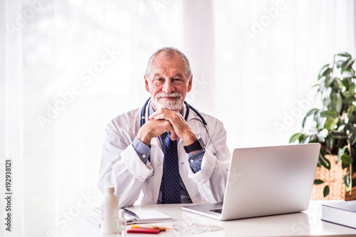 Senior doctor with laptop sitting at the office desk.