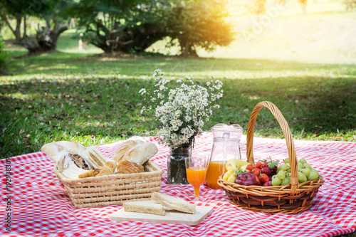Picnic Lunch Meal Outdoors Park Food Concept, Closeup of picnic basket with drinks, food and flowers on the grass.